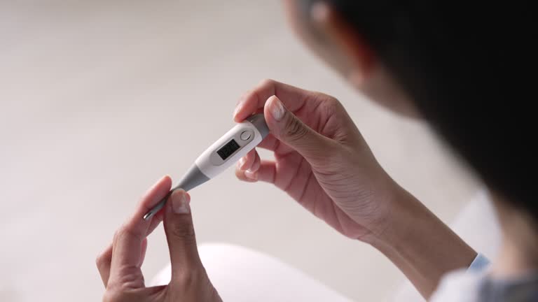 A close-up of a person holding a digital fever thermometer to check the body temperature.