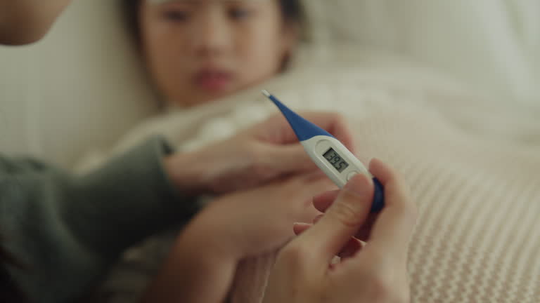 A parent holding a digital fever thermometer showing a high temperature of 39.5 degrees Celsius next to a sick child in bed.