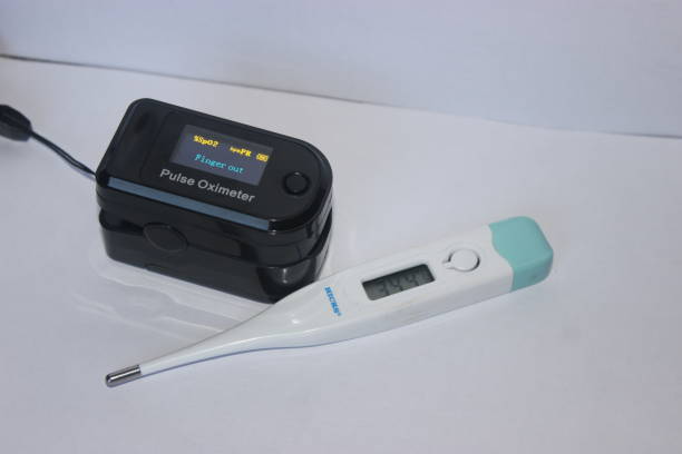 A black fingertip pulse oximeter showing 'Finger out' display status placed next to a white and blue digital medical thermometer on a plain surface.